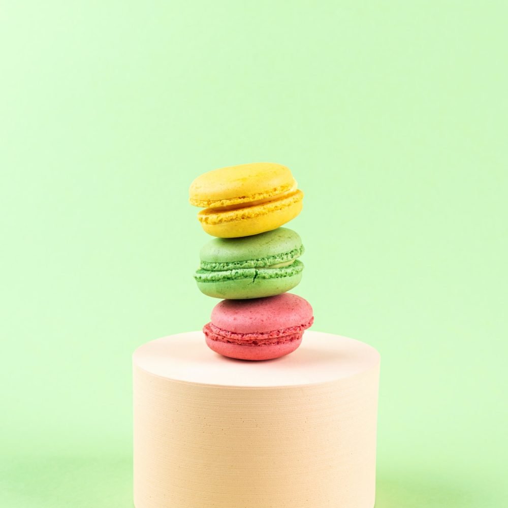 geometric-pastel-green-background-with-colorful-macaroon-sweet-candies-on-circle-podium.jpg